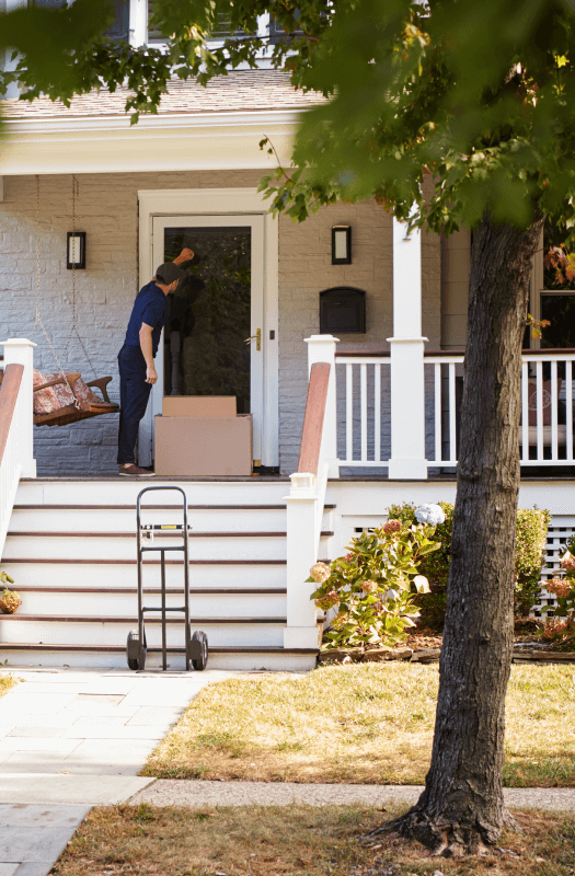 contact-us-img Interracial couple smiling while moving with cardboard boxes on a sunny day.