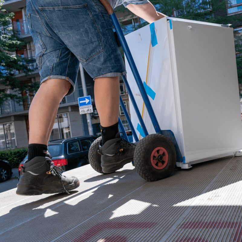 Interracial couple smiling while moving with cardboard boxes on a sunny day.